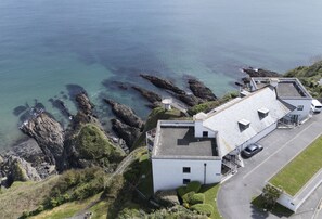 Ein Küstengebäude mit befestigter Auffahrt, einem kleinen Parkplatz und Blick auf das Meer.