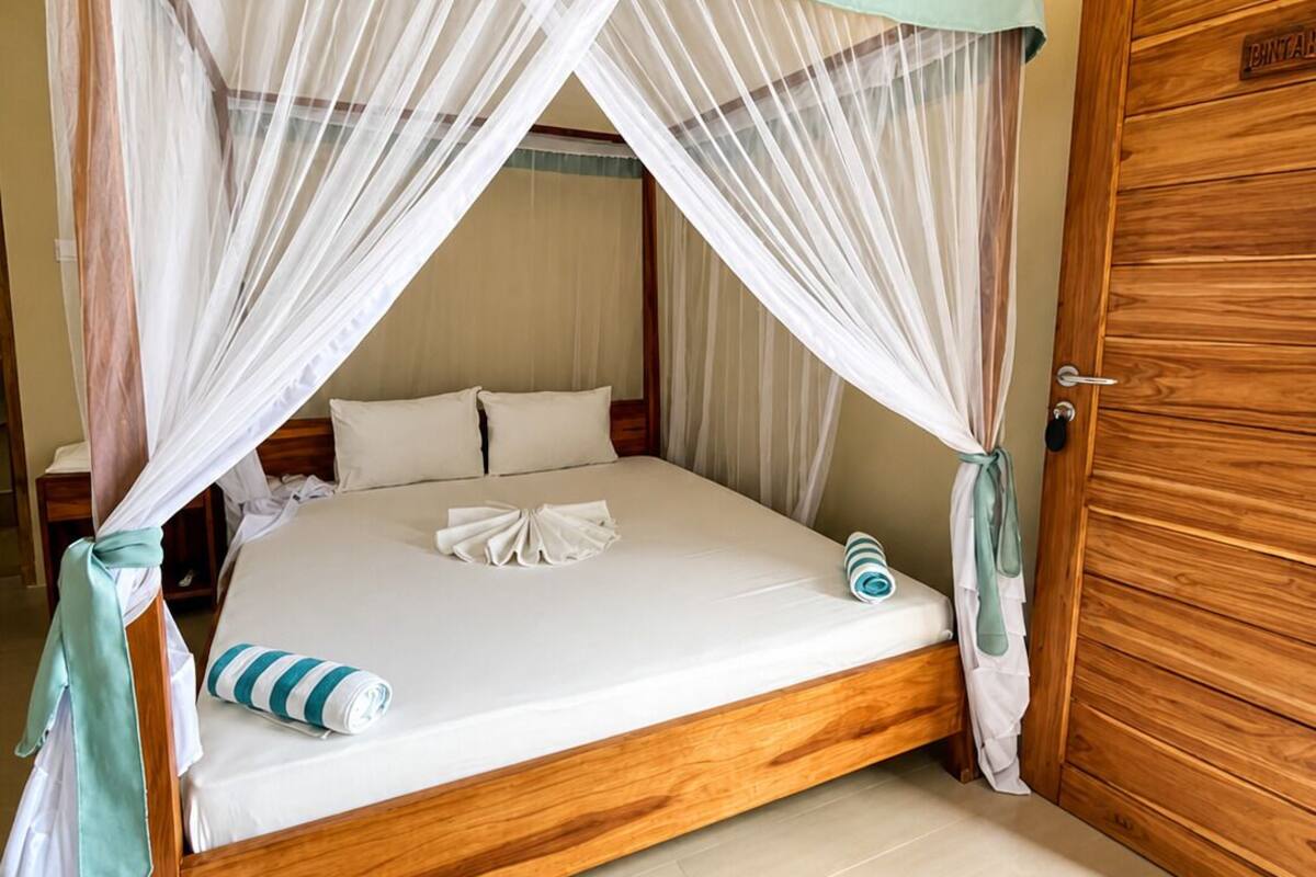 A single bed with a canopy, a wooden door, and a tiled floor.
