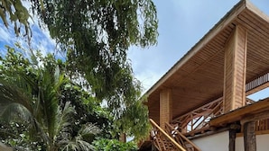 Edificio de madera con escaleras, rodeado de grava y follaje.