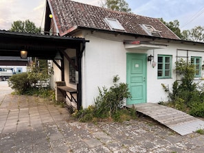Un pequeño edificio blanco con puerta verde, rampa y porche cubierto.