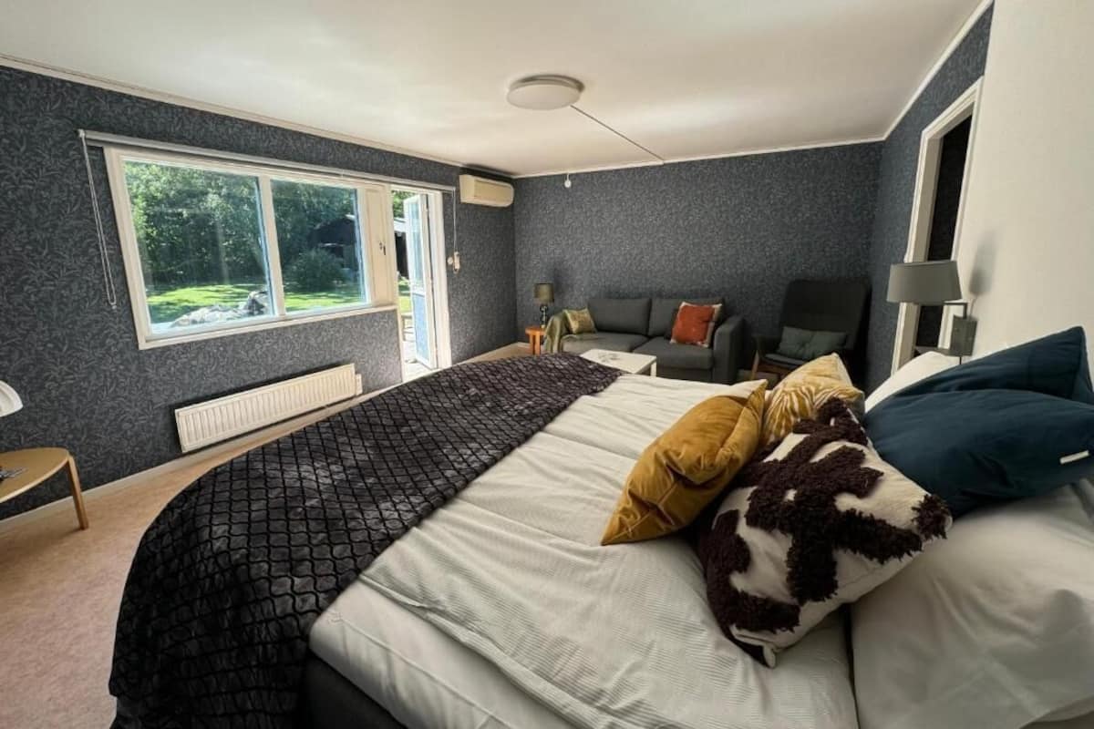 A bedroom with a large bed, a window, a radiator, a desk, and a chair.
