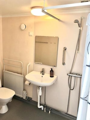 Un baño con inodoro, lavamanos, espejo, ducha y perchero para toallas.