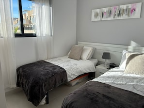 A bedroom with two beds, a nightstand with a lamp, a telephone, and a painting on the wall. - Penthouse Sabrina La zenia (Orihuela Costa)