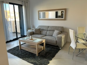 A modern living room with a sofa, a glass coffee table, a dining table with chairs, and a large mirror on the wall. - Penthouse Sabrina La zenia (Orihuela Costa)