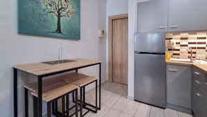 Eine moderne Küche mit einem Edelstahl-Kühlschrank, einem Holztisch mit zwei Stühlen und einem an der Wand hängenden Baum-Bild.