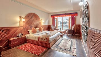 Habitación de hotel con una cama grande, un cabecero de madera, un rincón de descanso con sillones, una mesa de centro y vistas a la ciudad desde la ventana.