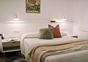 A hotel room with a bed, bedside tables, a nightstand, a lamp, and a wall-mounted picture. - COSY APARTMENT closed to RIVERSIDE & Parking (Bilbao)