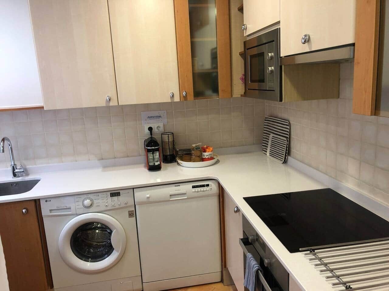 Een functionele keuken met een wasmachine, een magnetron en een fornuis.