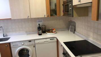 Een functionele keuken met een wasmachine, een magnetron en een fornuis.