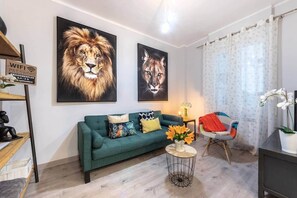 Ein Wohnzimmer mit einem grünen Sofa, zwei gerahmten Tierporträts, einem kleinen runden Couchtisch und einem Sessel mit roter Decke.