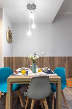 Ein Essbereich mit einem Holztisch, blauen Stühlen, einer Blumenvase und einer hängenden Leuchte.