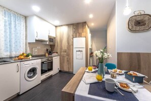 Eine kompakte Küche mit Mikrowelle, Backofen und Waschmaschine, ein Essbereich mit für das Frühstück gedecktem Tisch und einer Wanduhr.