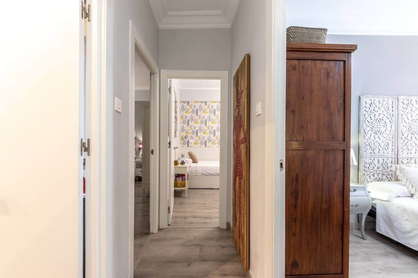 Ein Flur, der zu einem Schlafzimmer führt, mit einem Bett, einem Holzschrank und einer dekorativen Wandverkleidung.