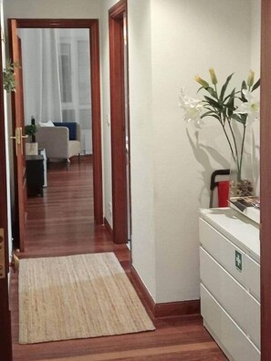 A hallway with a wooden floor, a white wall, and a small white cabinet with a green emergency sign.