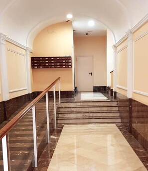 Eine Marmortreppe mit hölzernem Geländer führt zu einer Tür oben.