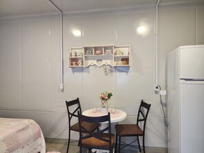 A small kitchenette with a white refrigerator, a table with two chairs, and a wall-mounted shelf with kitchenware. - Loft Comfort Couple between Beto Carrero, Balneário Camboriú-SC (Navegantes)