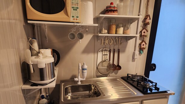 Cozinha compacta com micro-ondas, fogão, pia e diversos utensílios.