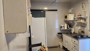 Uma cozinha compacta com geladeira, micro-ondas, fogão e uma pia pequena. Há uma cadeira e uma mesa com um vaso de flores.