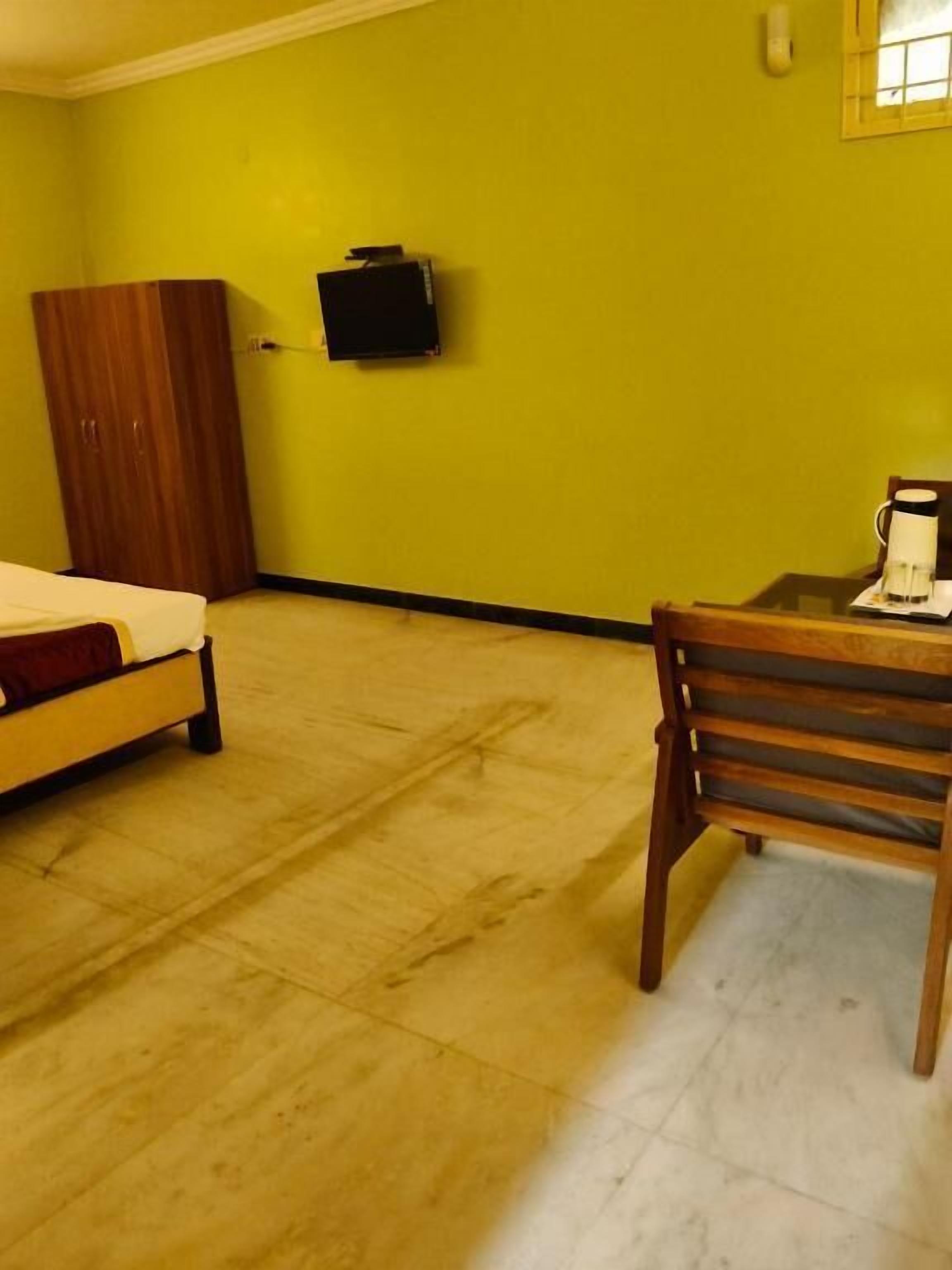 Una stanza con un letto, un tavolo di legno con una macchina del caffè, una televisione a parete e un armadio.