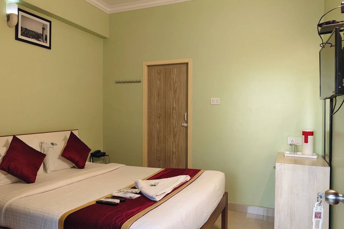 A hotel room with a bed, a wooden door, a television, and a bedside table with a glass and a container.
