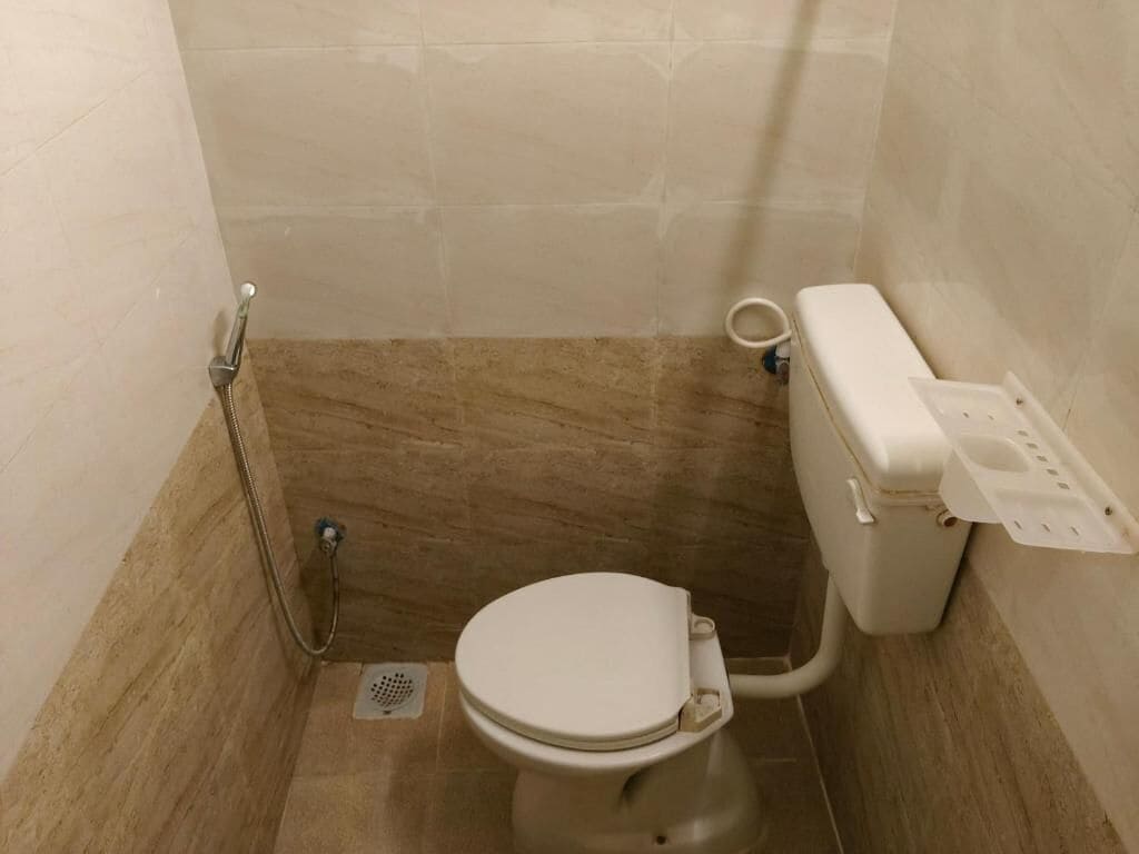 Un baño pequeño y funcional con inodoro, ducha y soporte de papel higiénico en la pared.