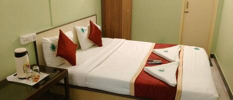 A neatly made bed with white and red bedding, a wooden wardrobe, a bedside table with a cup and glasses, and a mirror on the wall.