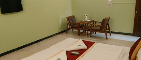 A hotel room with a bed, two chairs, a small table, a TV, and a door.