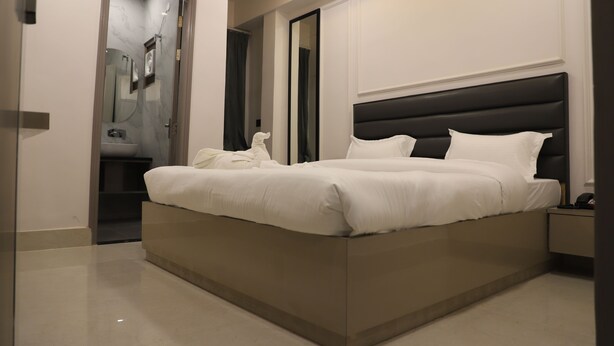 Une chambre à coucher moderne, avec un grand lit, une table de chevet, un miroir et une salle de bain visible à travers une porte ouverte.