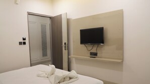 Une chambre d’hôtel avec un lit, un téléviseur fixé au mur et une porte donnant sur une autre pièce.