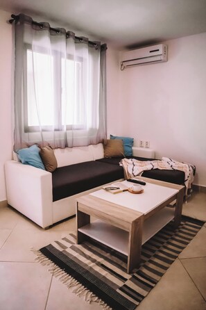 Ein Wohnzimmer mit einer Couch, einem Couchtisch, einem Fenster mit Vorhängen, einer Klimaanlage und einem gemusterten Teppich.