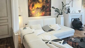 Un dormitorio moderno con una cama grande, un sofá blanco, una chimenea y un cuadro en la pared.