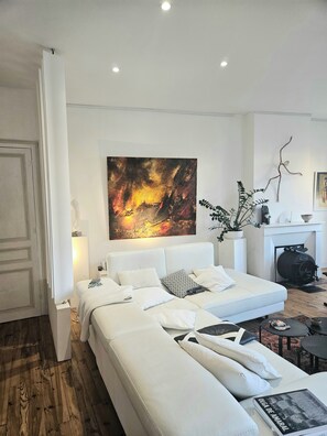 Une chambre à coucher moderne avec un grand lit, un canapé blanc, une cheminée et un tableau au mur.