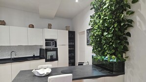 Una cocina moderna con armarios blancos, encimera negra, horno integrado, microondas y una pared con abundante vegetación verde.