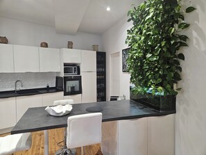 Une cuisine moderne avec des armoires blanches, un comptoir noir, un four encastré, un four à micro-ondes et un grand mur végétal.