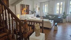 Un salón espacioso con una escalera de madera, un sofá blanco, un sofá negro y una chimenea.
