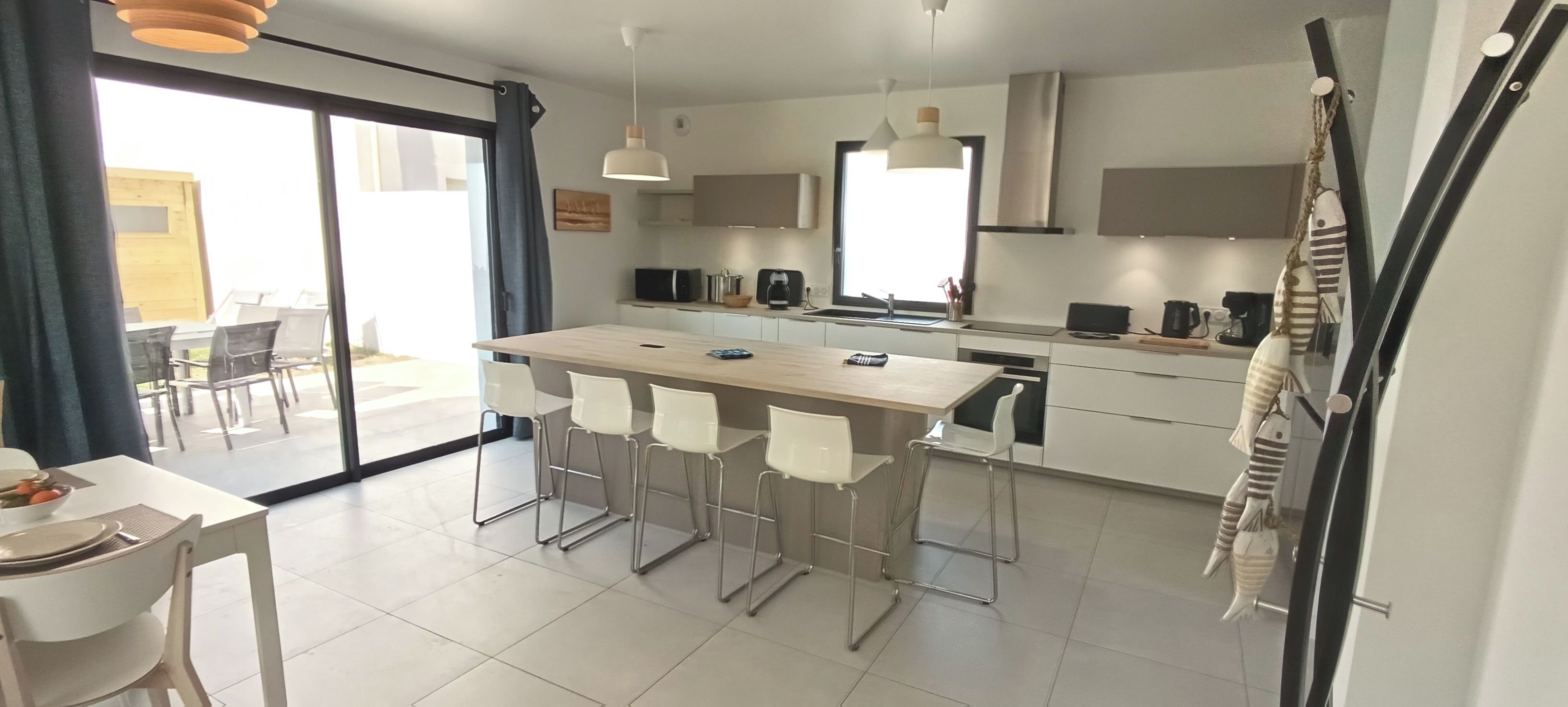 A modern kitchen with a central island, white bar stools, and a dining area with a table and chairs.
