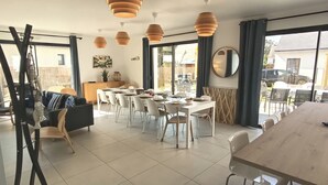 Uma sala de jantar com uma mesa comprida, cadeiras, luminárias pendentes e vista através de grandes janelas.