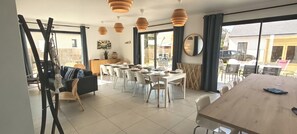 A dining area with a long table, chairs, pendant lights, and a view through large windows. - New house for 13 people. Sandy beach 3 minutes' walk (Bay). Sea views (Saint-Pierre-Quiberon)