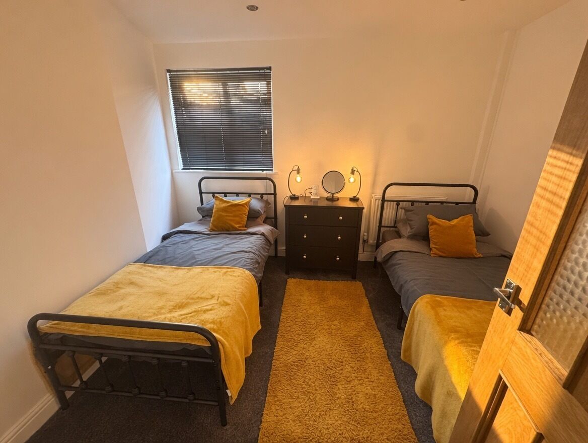 A bedroom with two single beds, a dresser, a window with blinds, and a door.