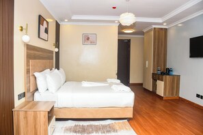 A hotel room with a bed, a wooden nightstand, a desk, a wardrobe, a television, and a kitchenette. - Sebai Luxury Suites (Naivasha)