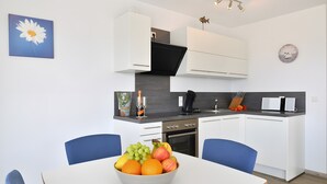 Uma cozinha moderna com armários brancos, um exaustor preto e uma fruteira sobre a mesa.