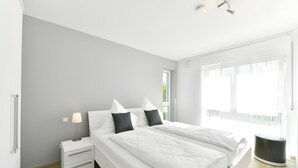 Quarto moderno com cama grande, mesas de cabeceira e janela com cortinas.
