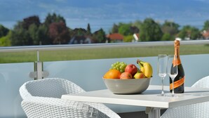 Uma mesa com uma tigela de frutas e dois copos, uma garrafa de champanhe, e vista para a paisagem.