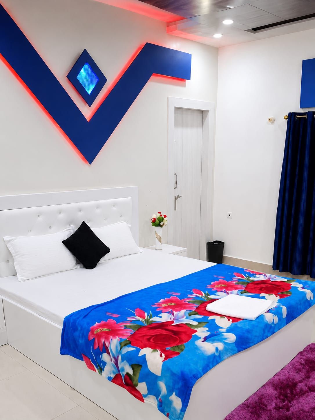 Un dormitorio con cama, mesita de noche, televisor montado en la pared y una puerta.