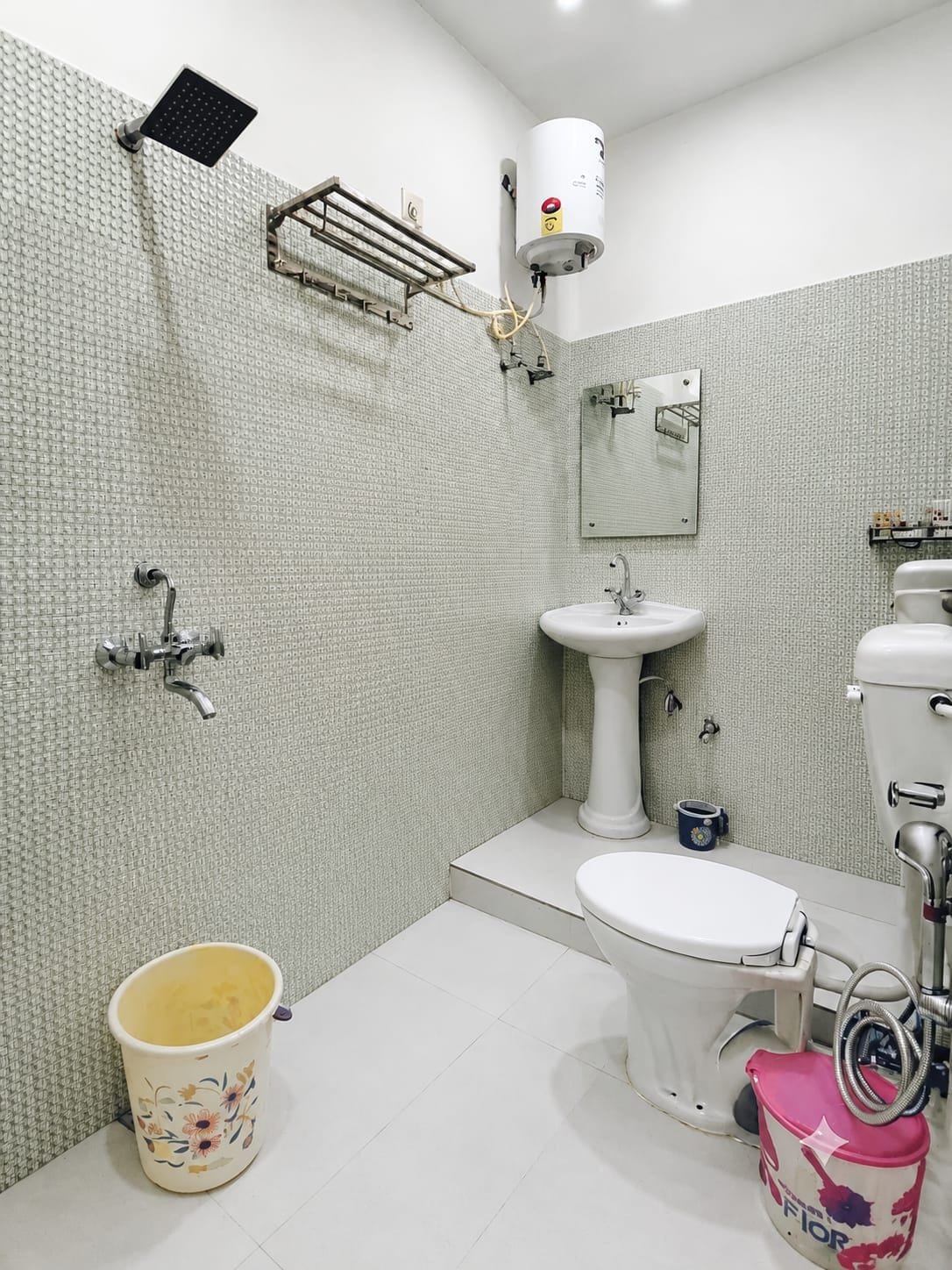 Une salle de bain équipée de toilettes, d’un lavabo, d’une douche et d’un chauffe-eau fixé au mur.