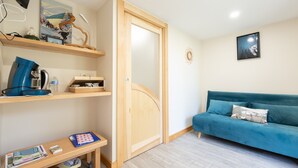 Una habitación con un sofá color turquesa, estanterías de madera, un escritorio con una máquina de café y una puerta de diseño curvo.