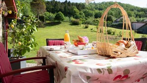 Mesa al aire libre con vista a un paisaje verde, una cesta de mimbre y una botella de jugo de naranja.