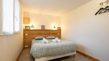 A bedroom with a wooden headboard, a bed with patterned bedding, a bedside table with a lamp, and a wall-mounted coat rack.