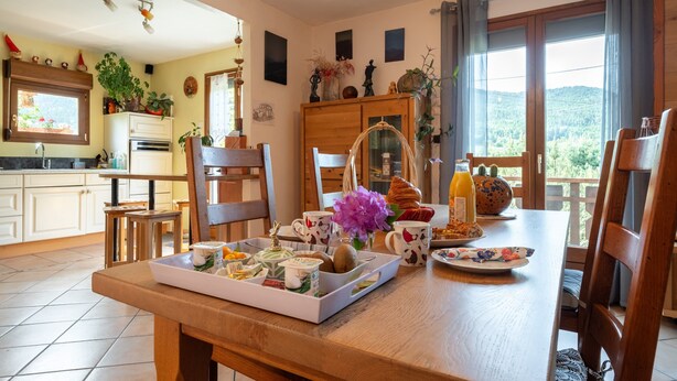 Un comedor con una mesa de madera preparada para el desayuno, una cocina al fondo y vistas al exterior.
