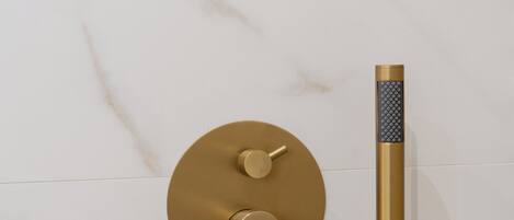 A modern shower with a gold faucet and control panel against a marble wall.